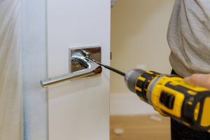 Carpenter installing door lock in the new house with a screwdriver