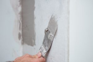 man hand with trowel plastering a wall, skim coating plaster walls